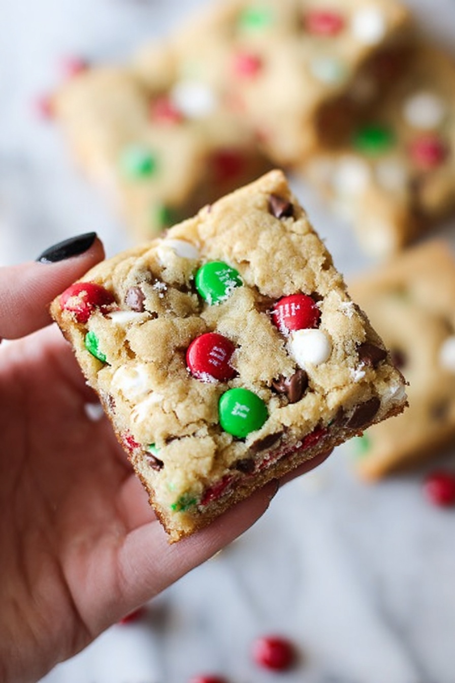 The image shows many square bars laid out neatly on a white marbled surface in a grid pattern. Each bar has a golden brown top layer that looks soft and slightly cracked. Embedded in the top layer are round candy pieces in bright red and green colors, along with small light beige nut pieces and tiny dark brown chocolate chips scattered across. The bars show a thick, darker brown base layer underneath the top. The overall look is colorful and festive with the mix of candies and nuts clearly visible on the surface. photo taken with an iphone --ar 2:3 --v 7